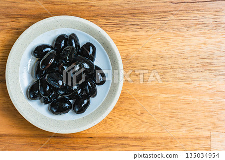盛在小碟子裡的黑豆,放在木桌上。 盛在小碟子裡的黑豆,放在木桌上。 135034954