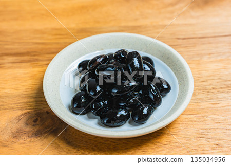 盛在小碟子裡的黑豆,放在木桌上。 盛在小碟子裡的黑豆,放在木桌上。 135034956