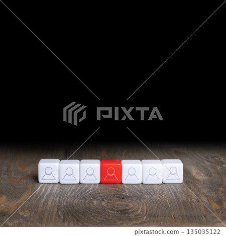 White and red blocks marked with a human figure icon are arranged in a row on a wooden surface against a black background. The red block signifies individuality. Concept of uniqueness 135035122