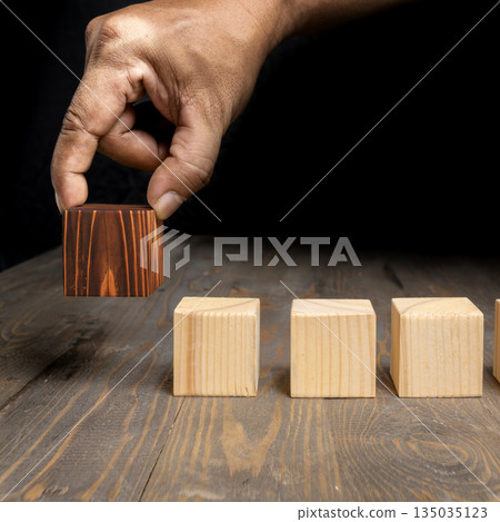 Hand placing a different color wooden cube in a row of similar cubes, symbolizing individuality, leadership, uniqueness, or standing out from the crowd. Concept of uniqueness 135035123