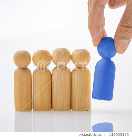 Wooden figures with one blue employee being picked from the group. Symbolizing individuality, leadership, uniqueness, or standing out from the crowd. Concept of uniqueness Wooden figures with one blue employee being picked from the group. Symbolizing individuality, leadership, uniqueness, or standing out from the crowd. Concept of uniqueness 135035125