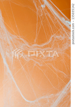 Spooky Halloween decoration with white cobweb on an orange background. Mockup, copy space, or template. Perfect for creating a festive atmosphere for Halloween parties or spooky projects 135035142