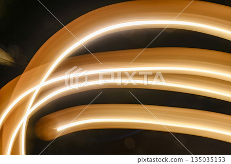 Abstract image featuring flowing light trails, creating curved lines with a warm, glowing tone. The light paints an organic, dynamic texture against a dark background Abstract image featuring flowing light trails, creating curved lines with a warm, glowing tone. The light paints an organic, dynamic texture against a dark background 135035153