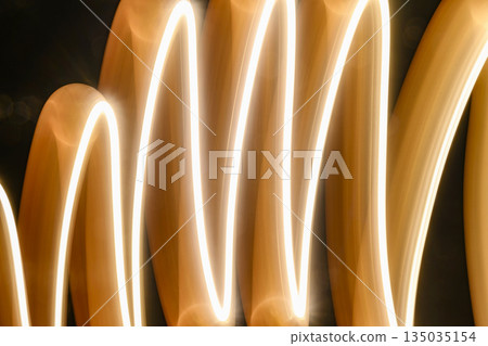 Abstract image featuring flowing light trails, creating curved lines with a warm, glowing tone. The light paints an organic, dynamic texture against a dark background Abstract image featuring flowing light trails, creating curved lines with a warm, glowing tone. The light paints an organic, dynamic texture against a dark background 135035154