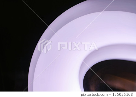 Abstract design featuring a glowing white pink circle shape against a stark, dark background. The soft lighting and smooth gradients create a sense of depth and visual interest 135035168
