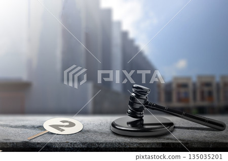 Gavel rests beside a numbered auction paddle on a textured table. City backdrop lends context to this scene, representing bidding and legal proceedings. Concept of auction 135035201