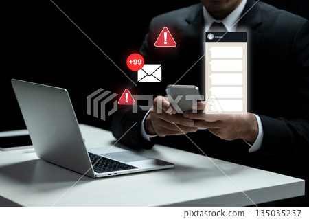 Businessman using a smartphone with a message notification and an email alert while working on a laptop. Concept of Scam Businessman using a smartphone with a message notification and an email alert while working on a laptop. Concept of Scam 135035257