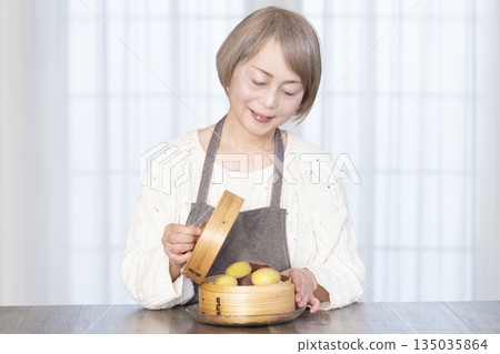 Senior woman eating steamed sweet potato in a bamboo steamer Senior woman eating steamed sweet potato in a bamboo steamer 135035864