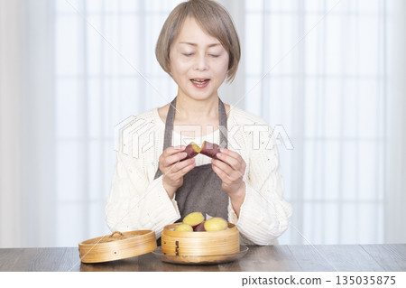 Senior woman eating steamed sweet potato in a bamboo steamer Senior woman eating steamed sweet potato in a bamboo steamer 135035875