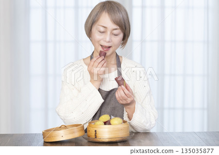 Senior woman eating steamed sweet potato in a bamboo steamer Senior woman eating steamed sweet potato in a bamboo steamer 135035877