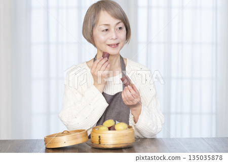 Senior woman eating steamed sweet potato in a bamboo steamer Senior woman eating steamed sweet potato in a bamboo steamer 135035878