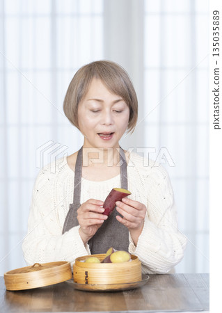 一位老婦人正在用竹蒸籠蒸地瓜。 一位老婦人正在用竹蒸籠蒸地瓜。 135035889