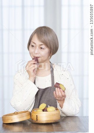 Senior woman eating steamed sweet potato in a bamboo steamer Senior woman eating steamed sweet potato in a bamboo steamer 135035897