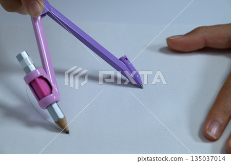 Close-up of a child's hand drawing a circle on a piece of paper with a compass Close-up of a child's hand drawing a circle on a piece of paper with a compass 135037014