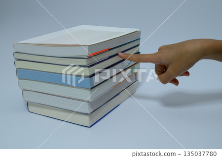 A hand pointing at a book in a pile A hand pointing at a book in a pile 135037780