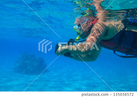 Man with photo camera taking photos and snorkeling underwater by coral reef in the Red sea, Egypt Man with photo camera taking photos and snorkeling underwater by coral reef in the Red sea, Egypt 135038572