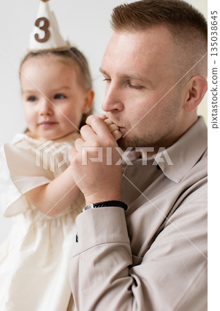 A loving father kisses his daughter's hand, celebrating her third birthday. The image captures a tender moment of family affection. 135038645