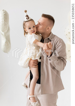 A father kisses his young daughter on the cheek while holding her during a birthday celebration. 135038651