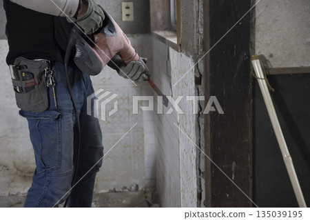 一名男工人試圖用電動鑿岩機移除瓷磚。 一名男工人試圖用電動鑿岩機移除瓷磚。 135039195