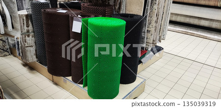 Rolls of anti slip rubber matting displayed in a retail store, featuring vibrant green, brown, and black colors for home and commercial use on tiled floor. Rolls of anti slip rubber matting displayed in a retail store, featuring vibrant green, brown, and black colors for home and commercial use on tiled floor. 135039319