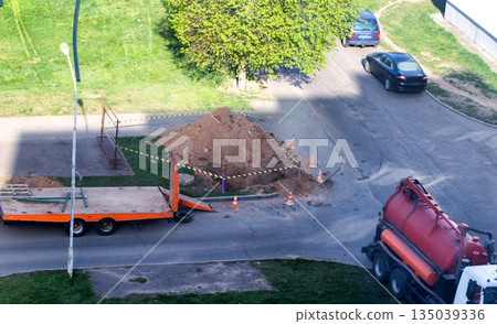 pumping tank against the background of a pit with a fence. Concept of liquidation of an emergency breakdown in a water supply system, copy space for text 135039336