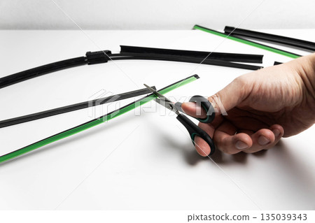Human hand uses scissors to trim new green rubber insert for car windshield wiper blade replacement process against clean white background studio shot Human hand uses scissors to trim new green rubber insert for car windshield wiper blade replacement process against clean white background studio shot 135039343
