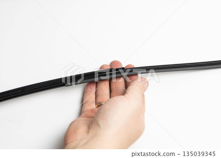 Hand holding car windshield wiper blade against white background, showing process of replacement of rubber insert on automotive accessory, maintenance of vehicle part Hand holding car windshield wiper blade against white background, showing process of replacement of rubber insert on automotive accessory, maintenance of vehicle part 135039345