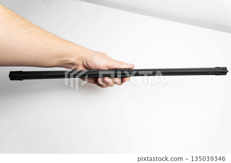 Hand holding rubber strip of car windshield wiper blade against white background, showing component for automobile maintenance and replacement 135039346