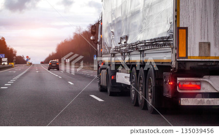 Large cargo truck drives along multilane highway road. Vehicle transport shipping logistics industry. Overcast sky day. Freight delivery distribution service. Copy space for text 135039456