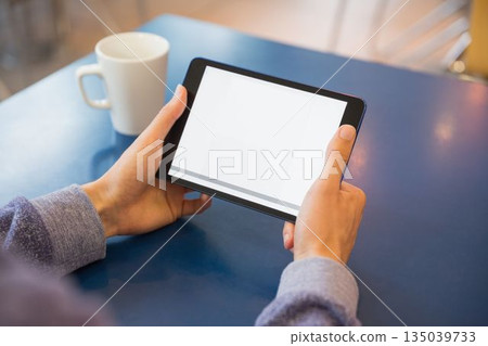Person is holding tablet with blank screen in flat-design coffee shop scene, with mug nearby 135039733
