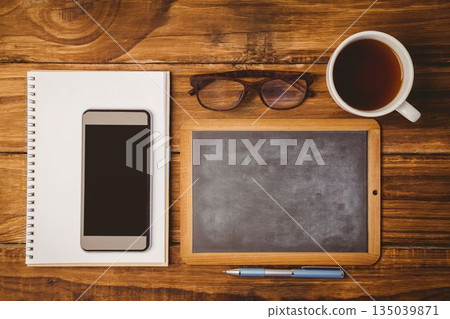 Showing flat-design overhead desk with pad and smartphone, framed chalkboard, glasses, coffee, pen 135039871
