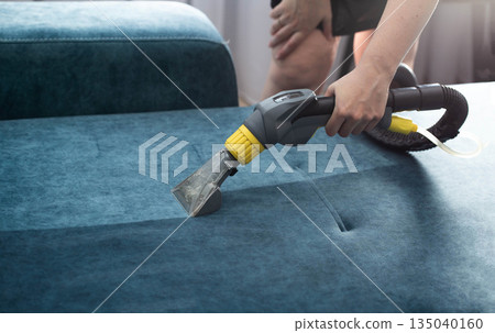 Cleaning a blue fabric couch using a professional upholstery cleaning machine in a bright living room Cleaning a blue fabric couch using a professional upholstery cleaning machine in a bright living room 135040160