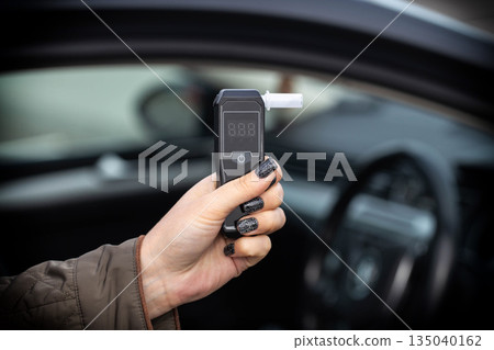 Hand With Manicure Holds Breathalyzer Inside Vehicle. Close-Up Of Sobriety Checking Device. Hand With Manicure Holds Breathalyzer Inside Vehicle. Close-Up Of Sobriety Checking Device. 135040162