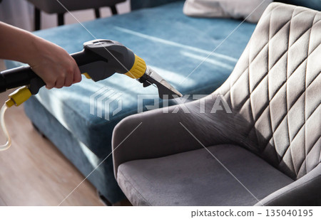Cleaning a fabric chair with a steam cleaner in a bright living room 135040195