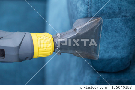 Cleaning a blue upholstered couch with a vacuum tool for deep upholstery care in a bright living room Cleaning a blue upholstered couch with a vacuum tool for deep upholstery care in a bright living room 135040198