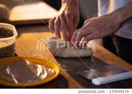 Person hands kneading bread dough on wooden surface preparing homemade baked food close up detail of culinary process home cooking baking food preparation 135040278