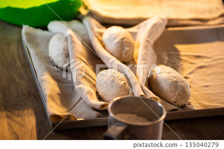 Raw bread dough loaves proofing on baking tray covered with linen cloth ready for baking artisanal whole grain sourdough rustic bread preparation process bakery kitchen table homemade food Raw bread dough loaves proofing on baking tray covered with linen cloth ready for baking artisanal whole grain sourdough rustic bread preparation process bakery kitchen table homemade food 135040279