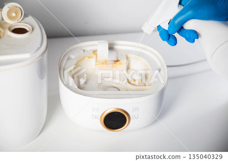 Spraying a chemical rust and scale remover into a humidifier. Home humidifier maintenance, close-up 135040329