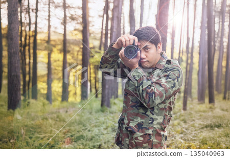 Asian male soldier taking photos with a DSLR camera in a forest. Military uniform, nature photography, military personnel, outdoor photography. 135040963