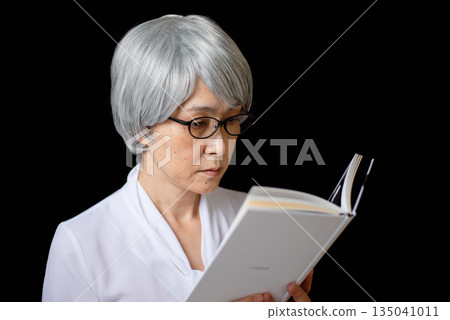 A gray-haired senior woman reading a book wearing reading glasses A gray-haired senior woman reading a book wearing reading glasses 135041011