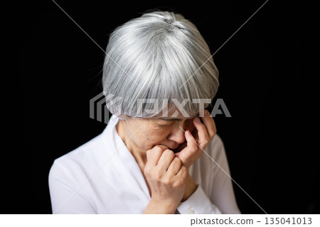 An elderly woman with grey hair is devastated and covers her face with her hands. An elderly woman with grey hair is devastated and covers her face with her hands. 135041013