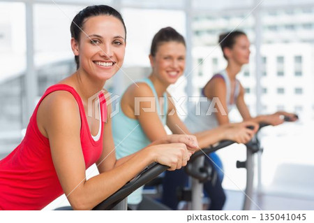 Three women are cycling in flat design fitness studio with city windows and exercise bikes Three women are cycling in flat design fitness studio with city windows and exercise bikes 135041045