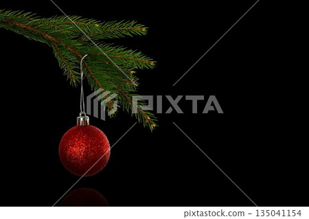 Flat design pine branch is extending, holding red glitter bauble against black backdrop, copy space 135041154