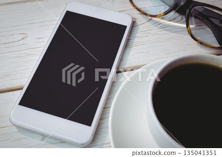 Flat design smartphone showing blank screen is lying on tabletop with coffee cup and glasses nearby Flat design smartphone showing blank screen is lying on tabletop with coffee cup and glasses nearby 135041351