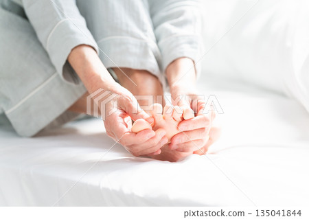A woman wakes up in bed with cramps in her legs A woman wakes up in bed with cramps in her legs 135041844
