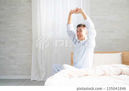 A man wakes up and stretches on his bed 135041846