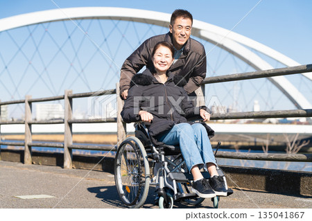 A middle-aged couple walking around pushing a wheelchair A middle-aged couple walking around pushing a wheelchair 135041867