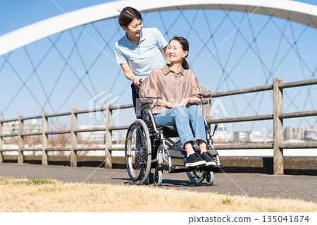 一名婦女和她的護理人員坐在輪椅上四處走動 一名婦女和她的護理人員坐在輪椅上四處走動 135041874