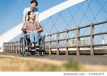 一名婦女和她的護理人員坐在輪椅上四處走動 一名婦女和她的護理人員坐在輪椅上四處走動 135041875