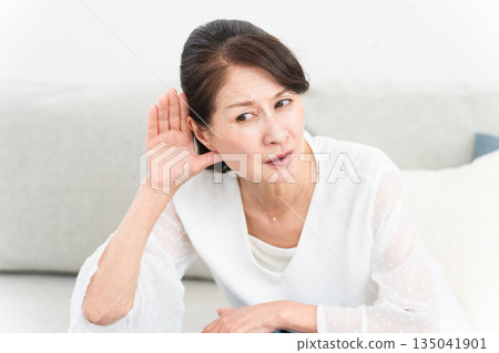 一位中年婦女用手摀住耳朵,聽著 一位中年婦女用手摀住耳朵,聽著 135041901
